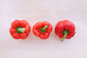 Vista cenital de tres pimientos rojos frescos dispuestos en fila sobre fondo claro. Imagen limpia, equilibrada y con colores vibrantes, perfecta para usos culinarios, editoriales o dise&ntilde;o gr&aacute;fico.
