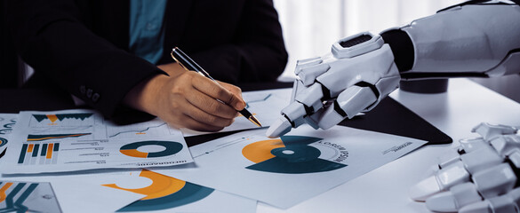 A human hand writing notes alongside a robotic hand, reflecting the integration of technology into business practices and its impact on teamwork and productivity.Noogenesis
