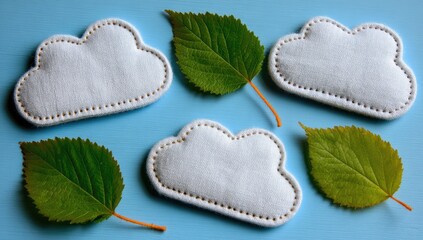 Four white felt cloud shapes, stitched with gold thread, arranged with vibrant green leaves on a light blue background