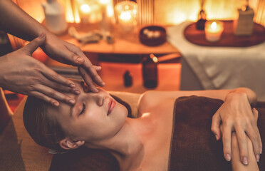 Caucasian woman enjoying relaxing anti-stress head massage and pampering facial beauty skin recreation leisure in warm candle lighting ambient salon spa in luxury resort or hotel. Quiescent