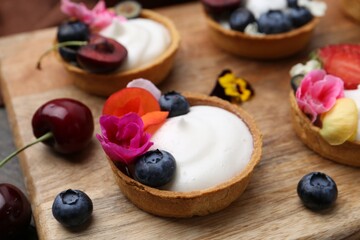 Sweet tartlets with berries and flowers on wooden board, closeup. Delicious dessert