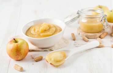 White bowl with homemade applesauce on wooden table. Yellow sauce in bowl and jar with almonds, apple. Healthy eating concept with natural ingredients. Baby food and vegetarian options.