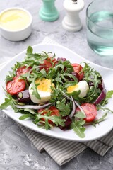 Tasty salad with arugula, vegetables and egg served on grey table, closeup
