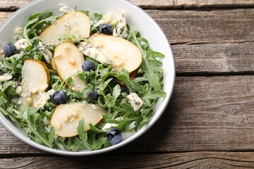 Tasty salad with arugula, pear, blue cheese, peanuts and blueberries in bowl on wooden table, above view. Space for text