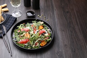 Tasty salad with arugula, cheese, grapefruit, vegetable and balsamic sauce on dark wooden table, closeup. Space for text