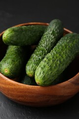 Fresh cucumbers in bowl on dark textured table, closeup