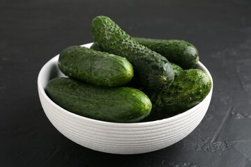 Fresh cucumbers in bowl on dark textured table, closeup