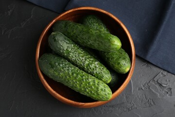 Fresh cucumbers in bowl on dark textured table, top view