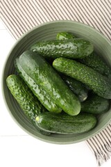 Fresh cucumbers in bowl on white wooden table, top view