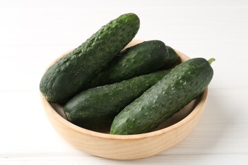 Fresh cucumbers in bowl on white wooden table, closeup