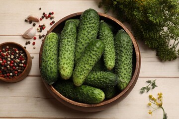 Making pickles. Fresh cucumbers in bowl, spices and dill on light wooden table, flat lay
