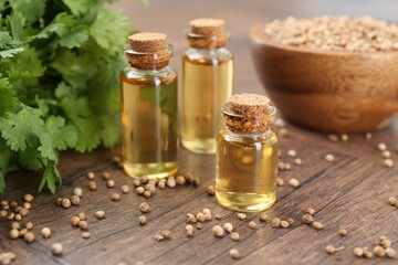 Aromatic oil in bottles, cilantro leaves and coriander seeds on wooden table, closeup