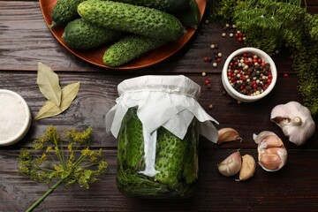 Pickled cucumbers in jar, fresh ones, garlic, dill and spices on wooden table, flat lay