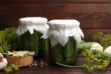 Pickled cucumbers in jars and spices on wooden table, closeup