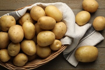 Fresh potatoes in basket on wooden table, flat lay