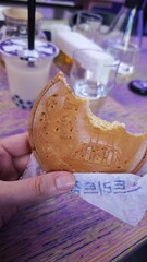 A hand holds a bitten Korean cheese-stuffed pancake over a vibrant table with bubble tea in the...