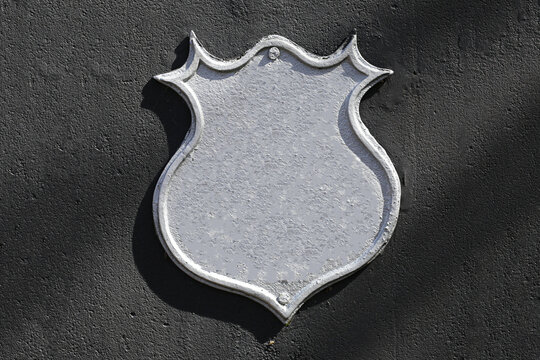 Blank metal shield sign. Empty silver plaque on dark wall. Copy space for custom text or logo. Vintage retro style emblem. Urban background for branding or signage. Industrial textured surface.