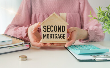 A woman is holding a wooden house that says Second Mortgage