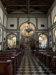 Fototapeta premium Palmanova, Italy - July 15, 2025: Interior view of historic church featuring wooden pews, ornate altar, and beautiful stained glass windows with copy space