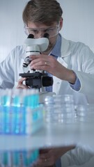 Male scientist researcher wearing lab coat and protective glasses, is using microscope in modern...