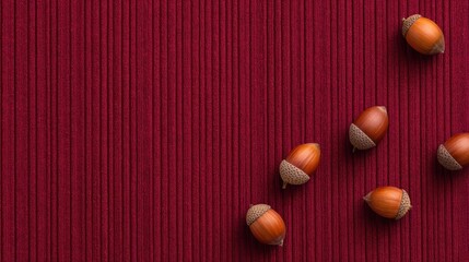 Acorns scattered on a textured red fabric background, creating a warm autumnal atmosphere