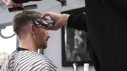 Professional barber trimming male client's hair using electric razor, creating precise haircut in contemporary barbershop setting with sleek styling tools