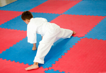 Young Kyokushin karate student performing a side split stretch on dojo mat, wearing a traditional...