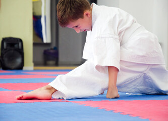 Young Kyokushin karate student performing a side split stretch on dojo mat, wearing a traditional...