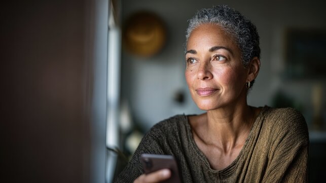 Focused medium view of a woman holding a smartphone during a virtual therapy session in a shelter gentle lighting and outoffocus room details conveying privacy and healing.
