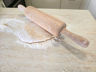Fresh dough, rolled out with a rolling pin on a floured surface, ready for baking. Food concept