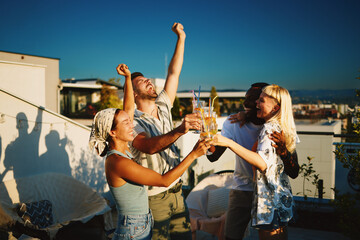 Cheerful friends are raising their cocktail glasses, enjoying a rooftop party at sunset