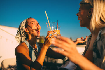Two women are sharing a moment of laughter while enjoying cocktails on a rooftop at sunset
