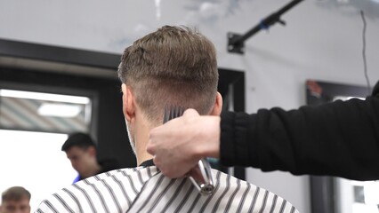 Professional hairstylist trimming client's hair using electric clippers, creating sleek, contemporary haircut with expert technique in modern barbershop setting