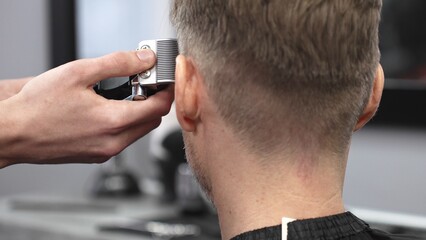 Skilled barber trimming client's hair with electric razor, demonstrating professional grooming technique in modern barbershop interior