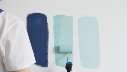 Painter wearing protective gloves rolling blue paint on white wall, creating gradient color effect for home interior renovation project © volha_r