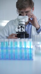 Male scientist researcher wearing lab coat and protective glasses, is using microscope in modern...