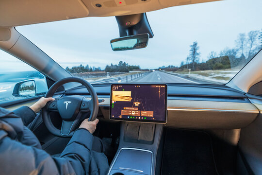 Female driver holding steering wheel of Tesla Model Y electric car with autopilot on winter highway. Sweden. Uppsala. 
