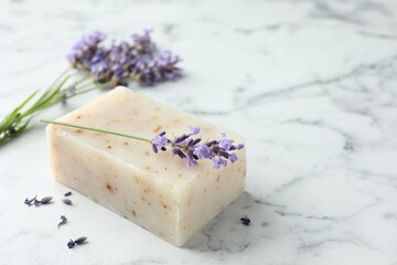 Soap bar and lavender flowers on white marble table, closeup. Space for text