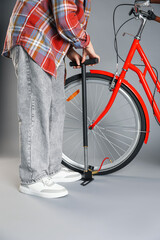 Woman inflating bicycle tire with manual air pump on grey background, closeup