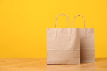 Two kraft paper bags on wooden table against orange background, space for text