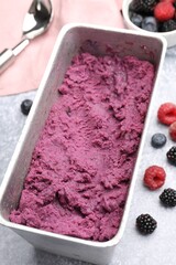 Delicious sorbet in metal container, fresh berries and spoon on grey table, closeup