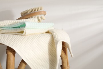 Folded waffle towels and massage brush on wicker chair near light wall, closeup
