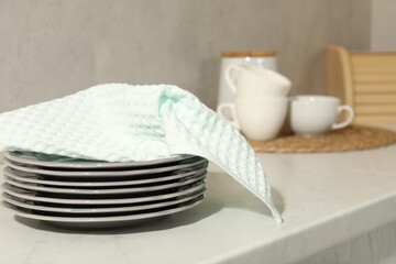 Waffle towel and stack of clean plates on white table near grey wall, closeup