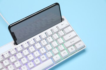 Modern white keyboard with RGB lighting and smartphone on light blue background, closeup