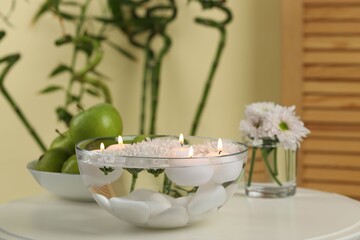 Burning candles and flowers in bowl of water on white table indoors