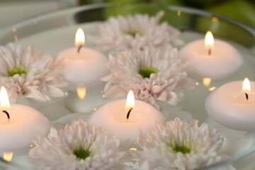 Burning candles and flowers in bowl of water as background, closeup