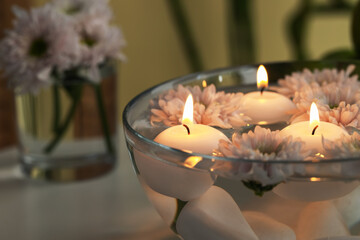 Burning candles and flowers in bowl of water on table indoors, closeup