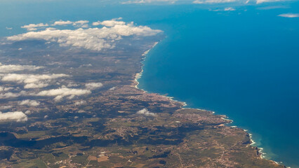 Aerial view of coastline and inland towns under scattered clouds