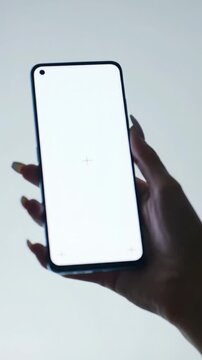 A pristine, high-resolution medium close-up video of a clean, gender-neutral hand holding a sleek, contemporary smartphone with a luminous white AMOLED screen, slowly micro-dolly zooming. Immaculate