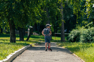 A boy rides a scooter through a park and looks to the right